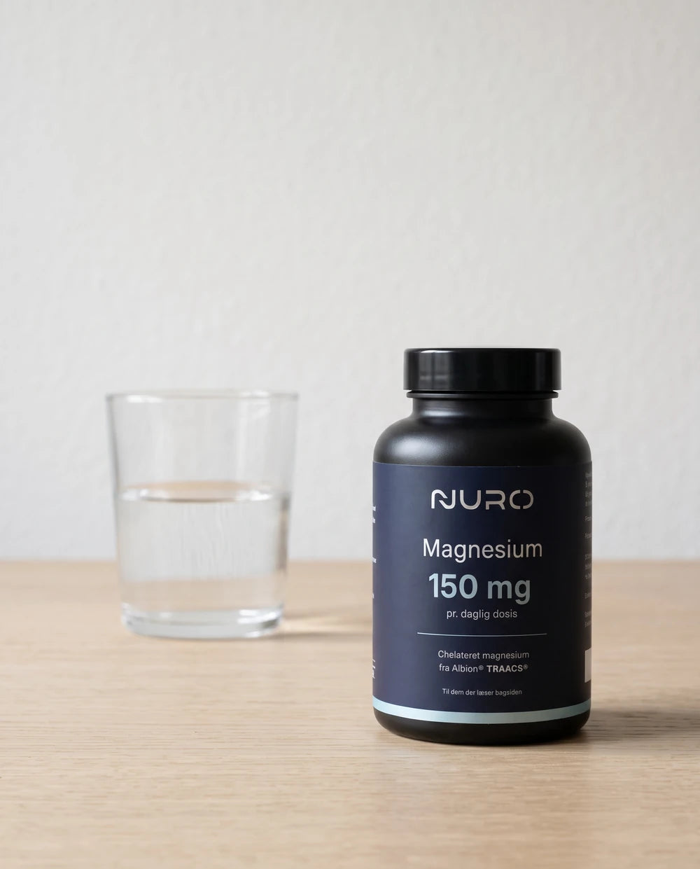 Nuro magnesiumflaske og et glas vand på lyst træ